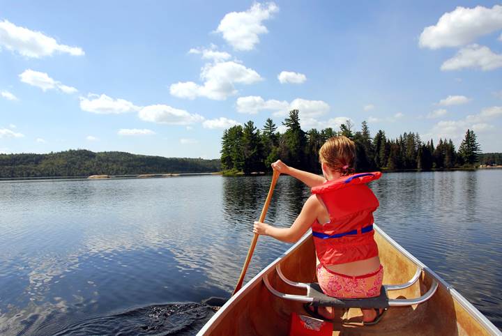 Foto på barn med röd flytväst som paddlar kanot på en sjö 