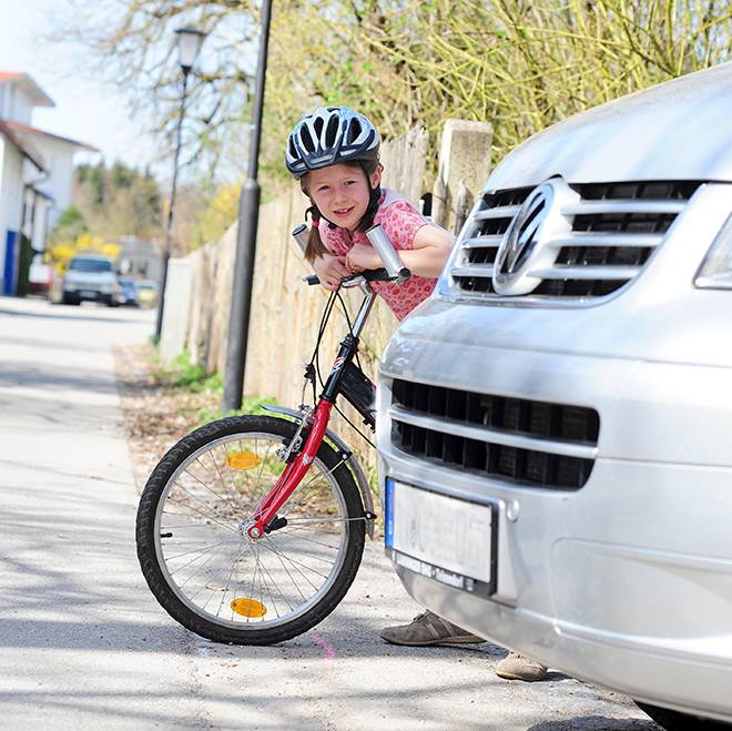 Foto på en flicka på cykel som kikar fram bakom en bil