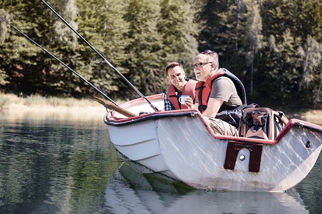 Två män sitter i en roddbåt med flytväst på sig och fiskar.