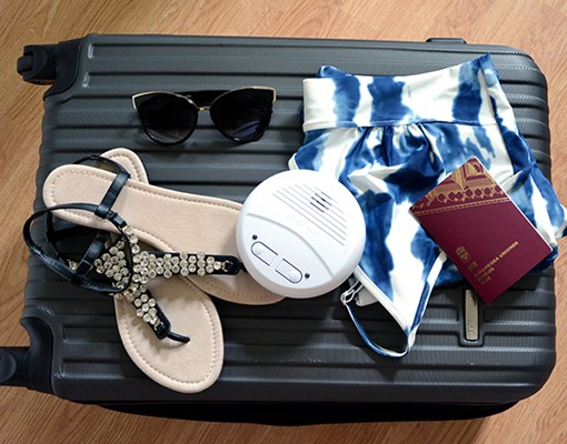 På en resväska ligger badkläder, sandaler, pass och en brandvarnare.
