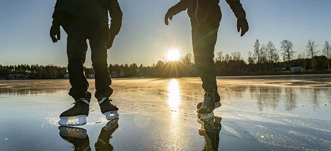 Två silhuetter som åker skridsko på en sjö.