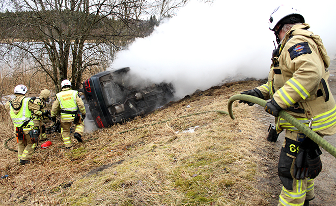 Brandmän släcker en bil som ligger på sidan och ryker